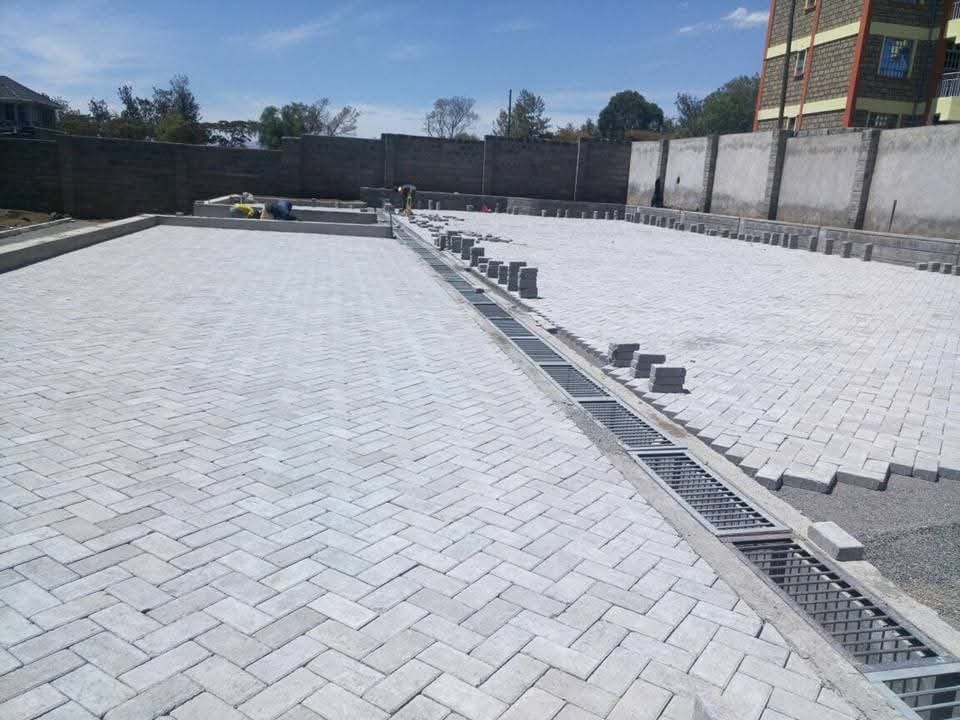 Drainage channel running through a herringbone Uni Paver compound in Kenya — UCB concrete drainage channel integrated into interlocking paving for surface water management