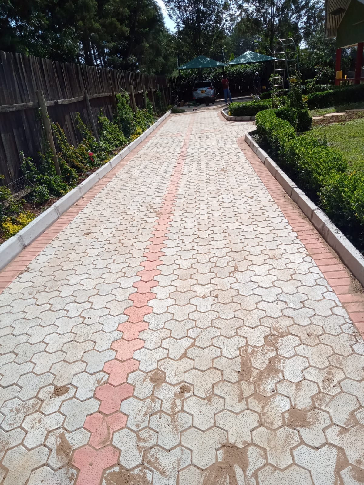 UCB Hexagon Cabro Pavers — smooth-finish hexagonal concrete pavers in grey with a red centre stripe installed along a manicured garden walkway in Kenya by Unique Concrete Builders